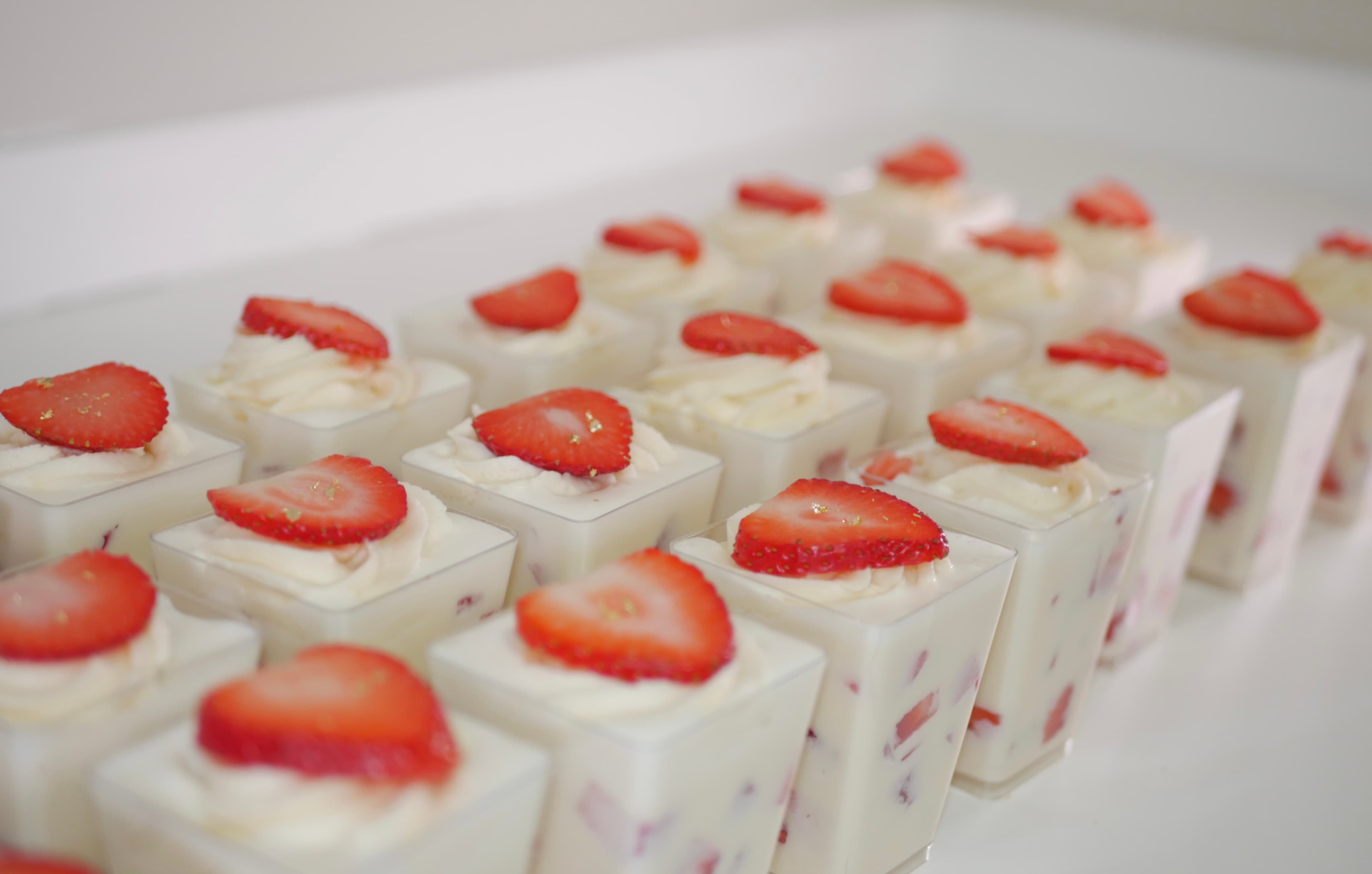 Rows of small square cups containing white cream dessert topped with fresh strawberry slices.